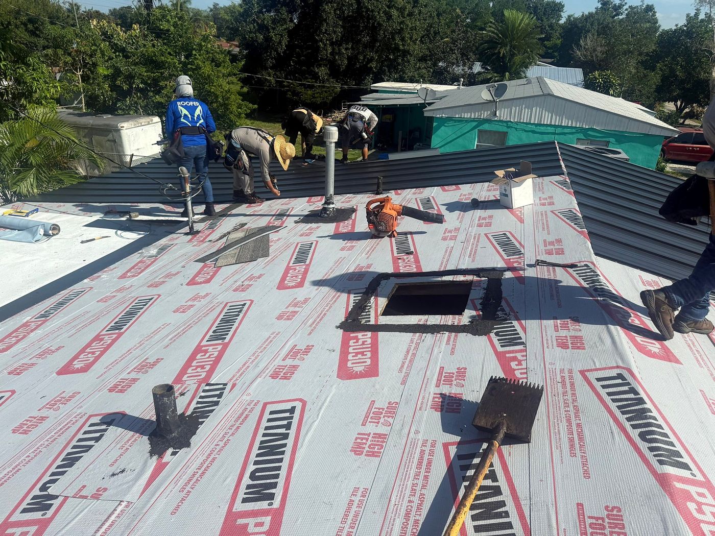 Crew installing a metal roof over synthetic underlayment, with vents and a skylight opening